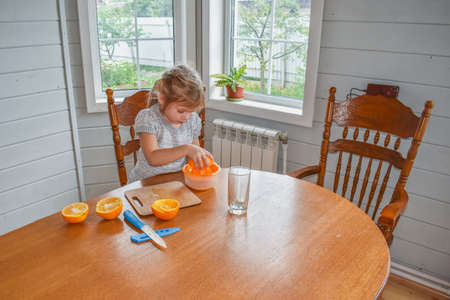 a child girl in the kitchen cuts and squeezes oranges juiceの写真素材