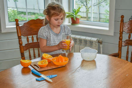 a child girl in the kitchen cuts and squeezes oranges juiceの写真素材