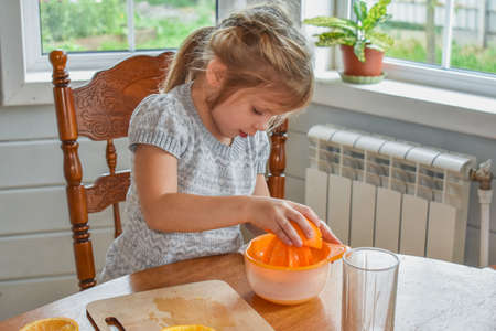 a child girl in the kitchen cuts and squeezes oranges juiceの写真素材