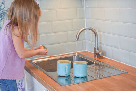 a child washes mugs in the sink photo without a filterの写真素材