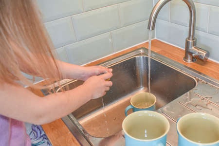 a child washes mugs in the sink photo without a filterの写真素材