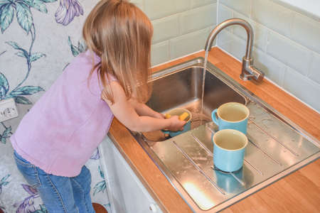 a child washes mugs in the sink photo without a filterの写真素材
