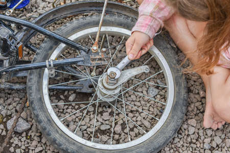 a child girl has damaged a bicycle wheel and is making repairs photo without processing