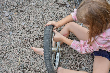a child girl has damaged a bicycle wheel and is making repairs photo without processingの写真素材