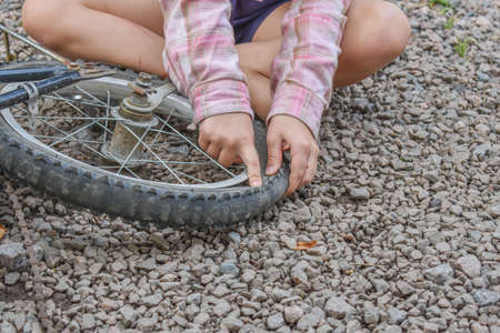 a child girl has damaged a bicycle wheel and is making repairs photo without processingの写真素材