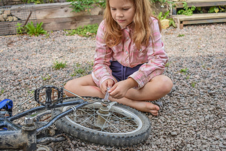 a child girl has damaged a bicycle wheel and is making repairs photo without processingの写真素材