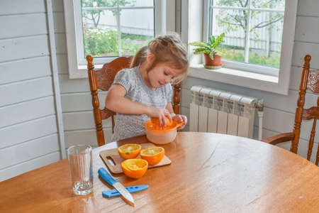 a child girl in the kitchen cuts and squeezes oranges juiceの写真素材