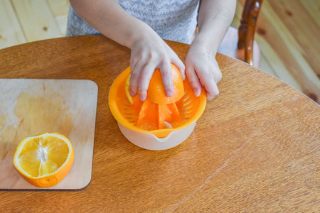 a child girl in the kitchen cuts and squeezes oranges juiceの写真素材