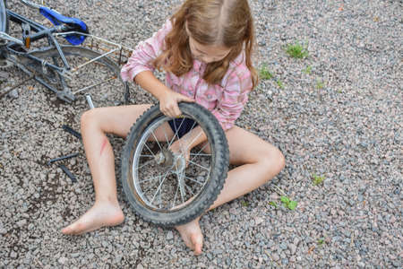 a child girl has damaged a bicycle wheel and is making repairs photo without processingの写真素材