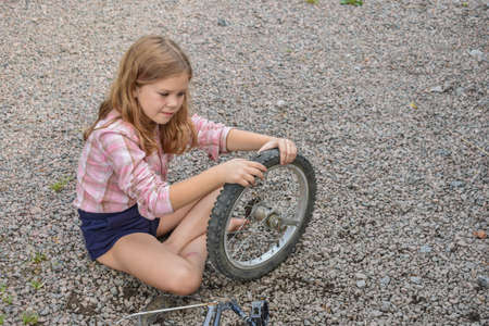 a child girl has damaged a bicycle wheel and is making repairs photo without processingの写真素材