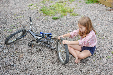 a child girl has damaged a bicycle wheel and is making repairs photo without processingの写真素材