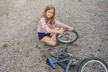 a child girl has damaged a bicycle wheel and is making repairs photo without processingの写真素材