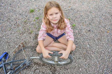 a child girl has damaged a bicycle wheel and is making repairs photo without processingの写真素材