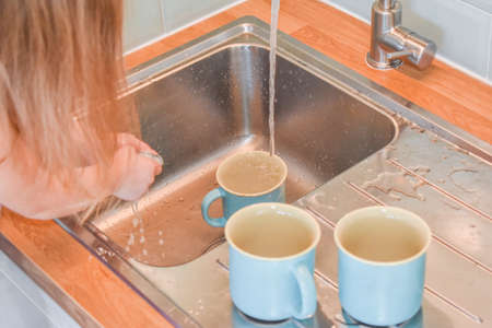 a child washes mugs in the sink photo without a filterの写真素材