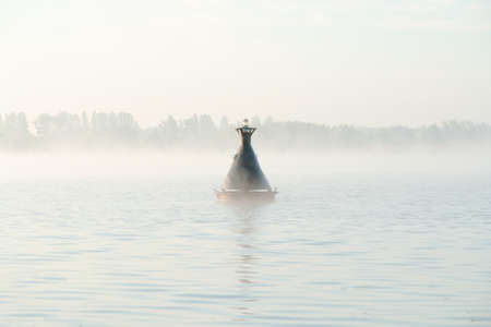 Rocking on waves of buoy in river in fog creates calm atmosphereの写真素材