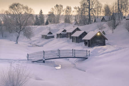 Cozy little houses on hill morning of winter village around frozen riverの写真素材