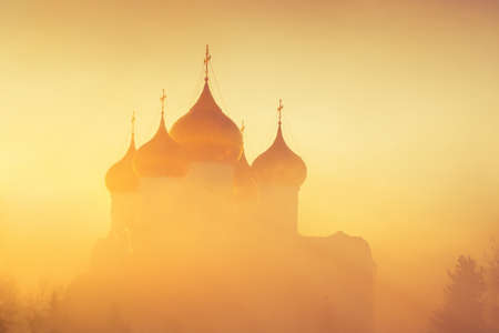 Golden domes in fog in sunlight as background. Winter frosty misty morning. Church in fog in background of rising sun.の写真素材
