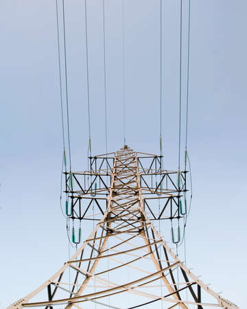 Lonely metal mast power lines with wires standing vertically from below against a blue sky day.の写真素材