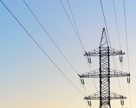 The tip end of the anchor supports of overhead power lines costs with wires and bundles of strands of high-voltage insulators against the clear blue sky.の写真素材
