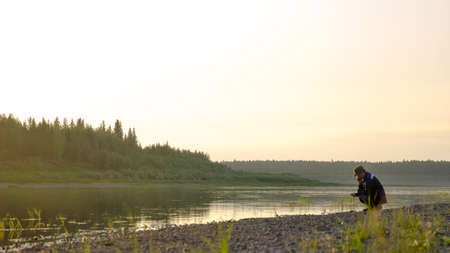 Young man Yakut squatting talking on a mobile phone on the banks of the wild Northern river vilyu in the taiga.の写真素材