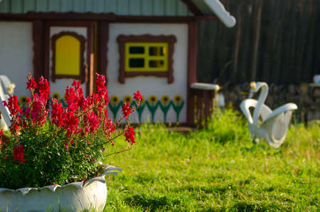 A flowerbed with bright colors from the tire stands on a green lawn against the background of a small house for children and a white Swan from a car wheel in the village of Northern Yakutia.の写真素材