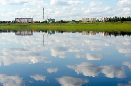 Construction of new multi-storey houses in the wild North of Yakutia in the village of Suntar in the afternoon with cranes and houses on the banks of the vilyu river with the reflection of clouds in the water.の写真素材