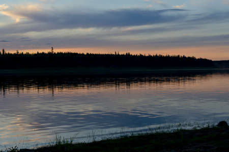 Bright blue sunset on the banks of the Northern river Viluy under the sky with clouds and a silhouette of spruce taiga in Yakutia.の写真素材