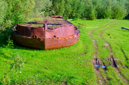 Abandoned bow of the rusty iron ship - the rest of the industry of the Soviet Union in the wild forests of the tundra of Yakutia lies on the road.の写真素材