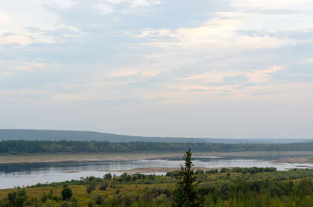 Lonely spruce on the plain near the Bank of the Yakut Northern river Viluy under the blue sky with mountains overgrown with forest.の写真素材
