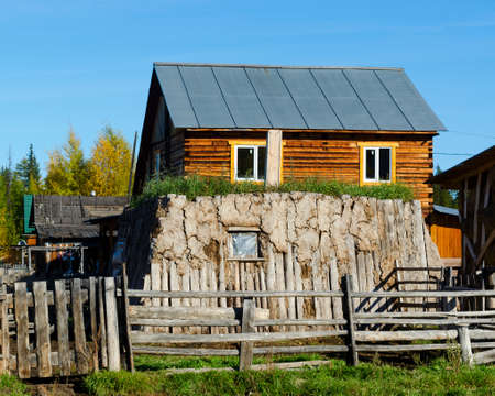The room for cattle khoton, made of cow dung and wood, overgrown with grass stands on a plot with a house made of pine in the North of Yakutia.の写真素材