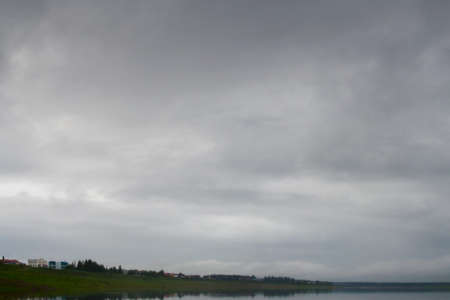 Fat gray clouds at sunset hang over the Northern rivers Viluy and houses of the village of Yakut Suntar.の写真素材