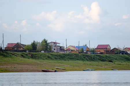 Boats are on the banks of the river Viluy at the cliff with the houses of the village of ulus Suntar in the North of Yakutia in Russia.の写真素材