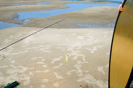 Photo shooting footage with fishing rod and bait Popper with reflector light and hand girl assistant on a sandy beach among the blue water in the summer.の写真素材