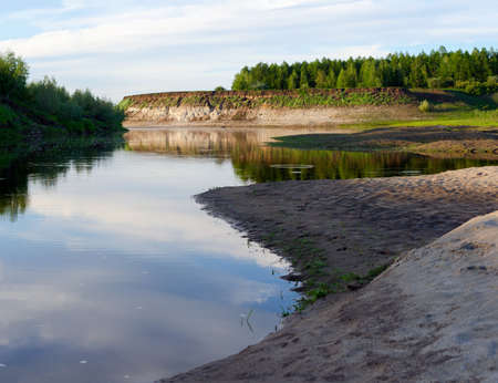 River Bank with sand in the shade at sunset before the cliff with spruce forest in the tundra of the wild North of Yakutia.の写真素材