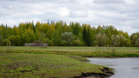 A lonely haystack behind the fence stands on the field near the pond in the wild taiga of the birch and spruce forest of Yakutia under the clouds in the autumn. The agriculture of the Northern peoples.の写真素材