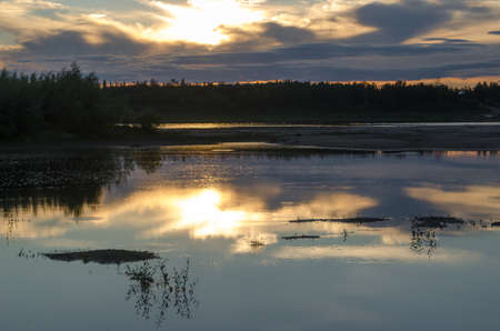 Bright sunset on the banks of the Northern river Viluy at sunset under the blue sky in the spruce forest and the silhouette of a car vacationer.の写真素材