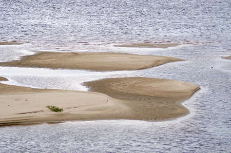 Parts of the sandy shore filled with rippling water of the river under daylight.の写真素材