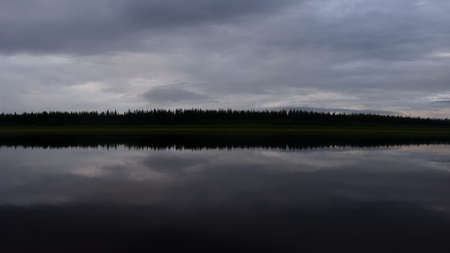 A dark strip of the silhouette of the spruce wild Northern forest in Yakutia between the reflection of the clouds in the evening at sunset.の写真素材