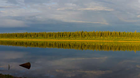 The remains of iron protrude from the surface of the water with the reflection of the strip of the Northern Yakut picturesque forest at sunset in the evening.の写真素材