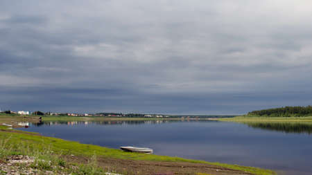 The boat is on the shore of the stone turning wild North of the river Vilyui bright in the evening on the background of the houses of the village the village of ulus Suntar.の写真素材