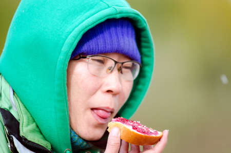 Yakut Asian girl eating sandwich bread with jam closing her eyes with pleasure on the background of flying snow flakes.の写真素材