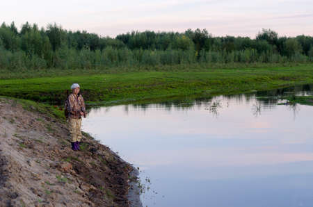 Yakut Asian girl-the tourist-fisherman with a backpack is fishing on the river Kempendyay from the sandy hills of the wild North spruce tundra of Russia.の写真素材
