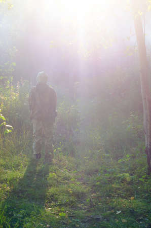 The girl froze and lowered his hands in protective clothing is looking up at the bright white light falling through the trees. Aliens take a UFO numb man.の写真素材