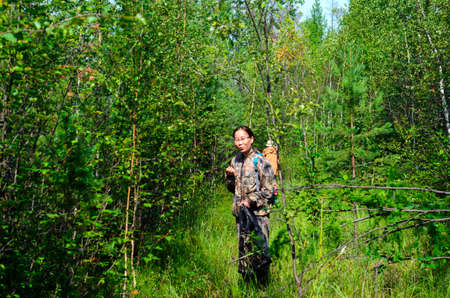 Girl tourists Asian gatherer of mushrooms in Yakutia with a package in his hands standing on a path in the woods, trying to taste the wild berries.の写真素材