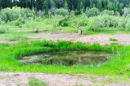 Yakut Asian girl tourist holding a package in his hand waving his hand standing behind a small pond after collecting wild onions.の写真素材