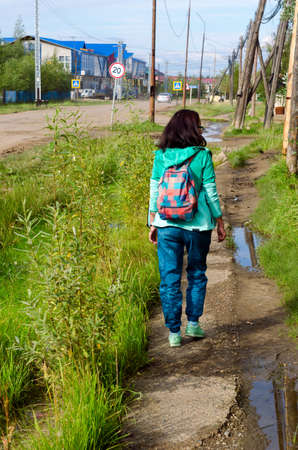 Yakut sporty girl with backpack light walk goes along the old sidewalk North of the village Suntar.の写真素材