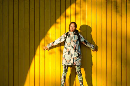 Beautiful Yakut young girl model sensually pressed her hands to the yellow wooden wall in the bright sun next to the semicircle shadow.の写真素材