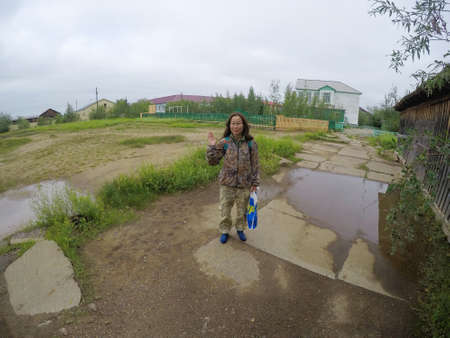 A young Yakut woman waving a welcoming hand standing with service on the old school site in the Northern settlement of Yakutia, Suntar.の写真素材