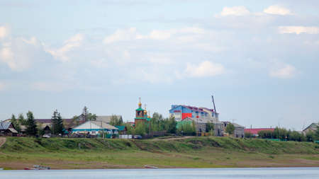 Houses with silhouettes of cars on the road near the cliff of the Northern vilyu river go to the Orthodox Church with Golden domes among the houses in the wild North of Yakutia in the ulus Suntar.の写真素材