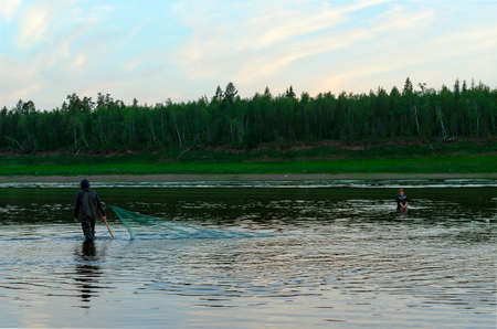 Two men Yakuts go in wading boots with fish net on the wildlife in the river Vilyuy in a forest taiga traditionally catching the local fish tugun.の写真素材